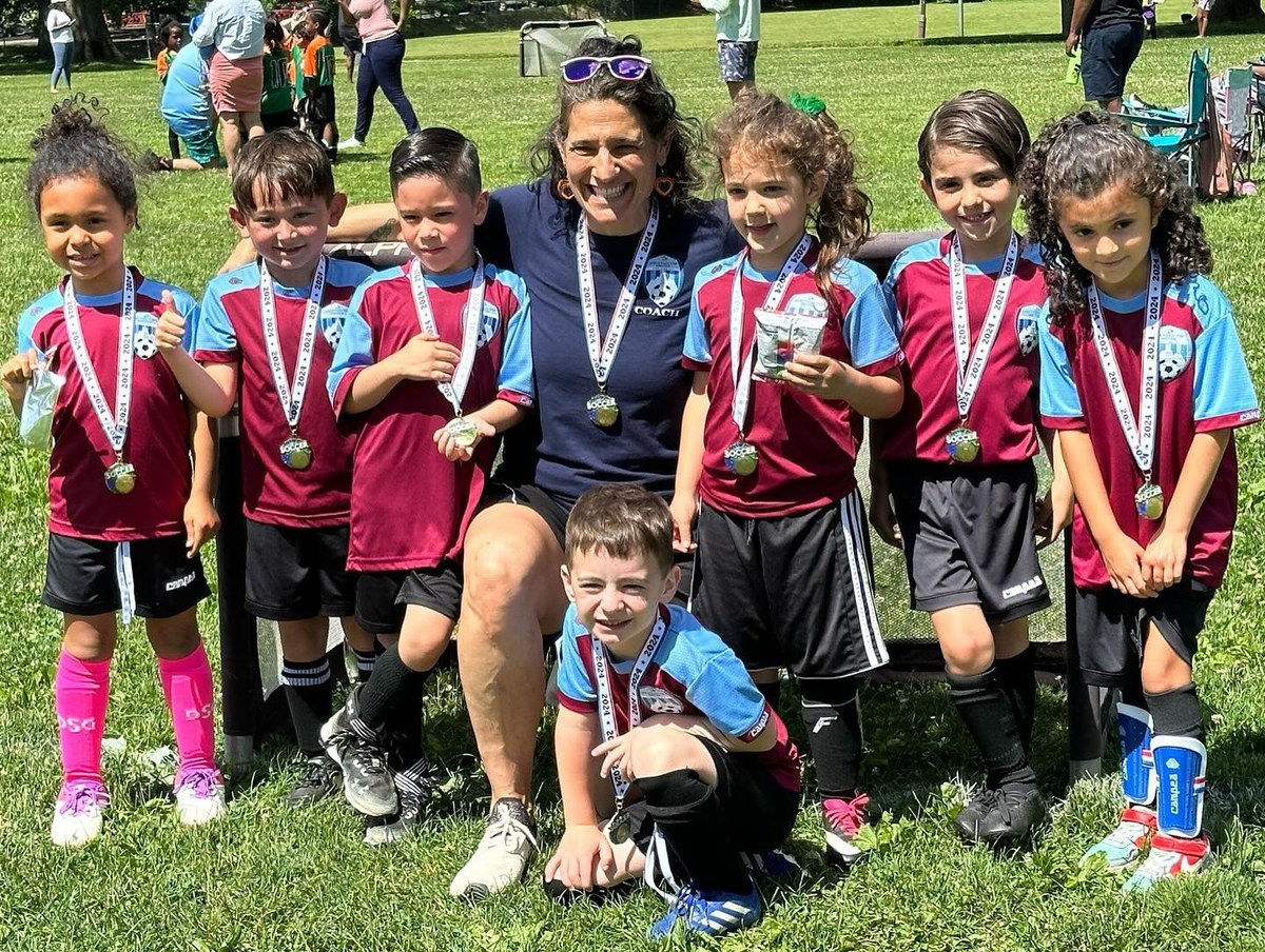 An MTL soccer team and their coach smiling with their season medals on a sunny field